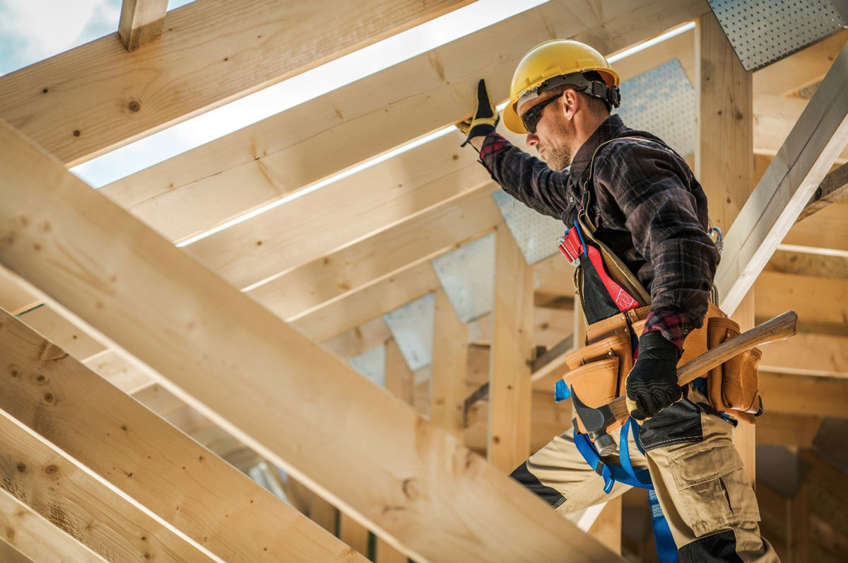 a man with hard hat and tools on roof beams