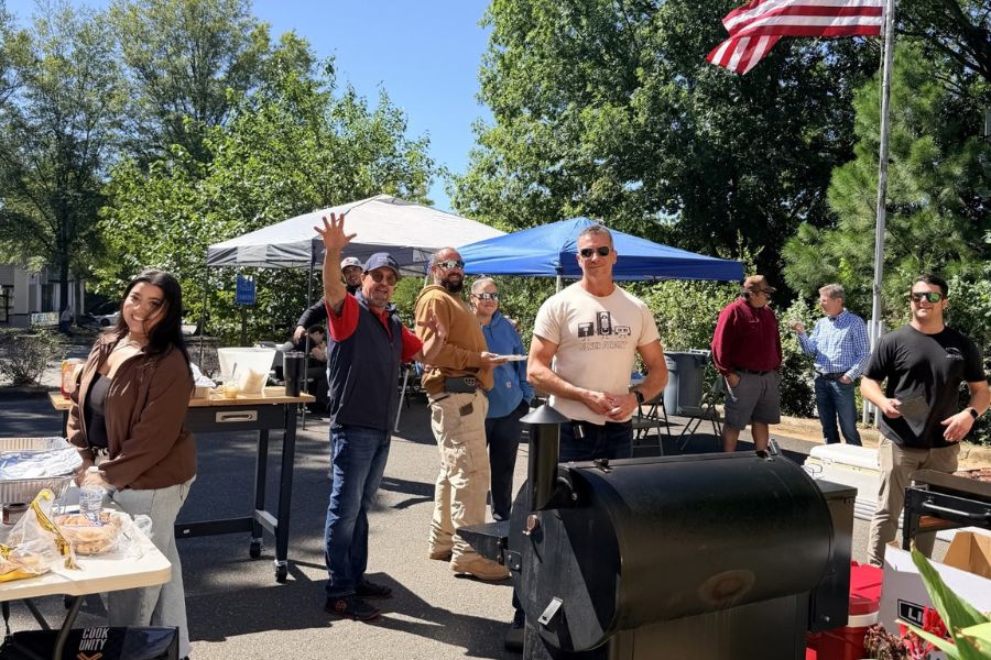 Attendees enjoying the outdoor barbeque on a sunny day waving at the camera